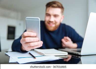 Happy man sitting at the table and using smartphone. Focus on smartphone