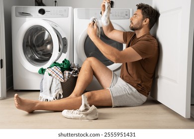 Happy man sorting clothes near washing machine in laundry room. man sits on the floor of a house near a washing machine with dirty clothes. a man does his laundry at home. a man holding dirty clothes - Powered by Shutterstock