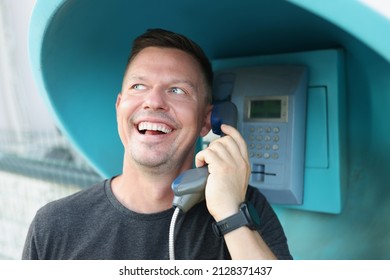 Happy man speaks on a public payphone on the street, close-up. Lack of mobile connection, phone call in the countryside