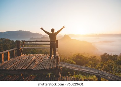 Happy Of Man Standing Alone With Arms Raised Up  During Beautiful Sunrise At The Morning.Enjoying With Nature