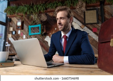 Happy Man In Suit Working On Laptop And Looking Away In A Coffeeshop