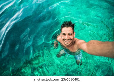 Happy man taking selfie with smart mobile phone device swimming in the ocean - Smiling tourist enjoying summer holiday outdoors - Summertime vacation and technology concept