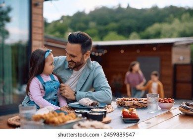 Happy man talking to his small daughter while having lunch at dining table on a patio.  - Powered by Shutterstock