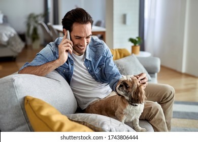 Happy Man Talking On Mobile Phone While Enjoying With His Dog On The Sofa.