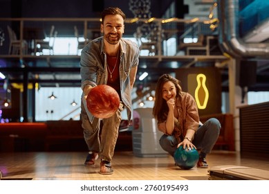 Hombre feliz que lanza una pelota mientras que juega con su novia en la bolera. 