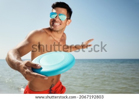 Happy man throwing flying disk at beach on sunny day