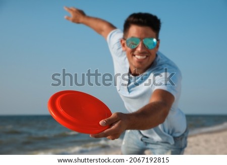 Happy man throwing flying disk at beach, focus on hand