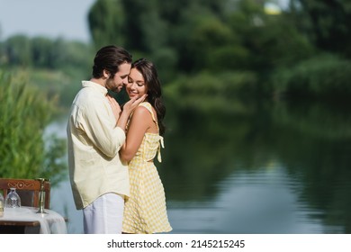 Happy Man Touching Cheek Of Smiling Woman Near Lake