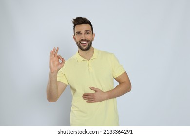 Happy Man Touching His Belly And Showing Okay Gesture On Light Background. Concept Of Healthy Stomach