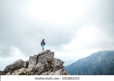 Happy man traveler with camera at the edge of a cliff in mountains. Travel and lifestyle concept. - Shutterstock ID 1053852191