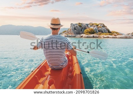 Happy man traveler kayaks near an ancient sarcophagus and a Lycian tomb in the flooded city of Kekova in Turkey. A pleasant and healthy vacation on the coast
