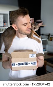 Happy Man Unpack Online Home Food Delivery. Abyssinian Cat Lying On Its Shoulders. Box With Packed Tuna, Shrimp, Vegetables And Recipe Card On A Kitchen Background. Food Delivery Services. Dinner Set.