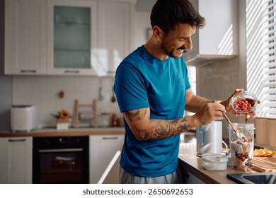 Happy man using blender while preparing fresh fruit smoothie in the kitchen. Copy space.