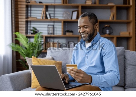 Happy man using credit card and laptop for online shopping. Relaxed atmosphere in a modern living room interior.