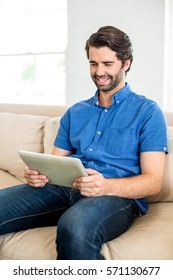Happy man using digital tablet while sitting on sofa at home