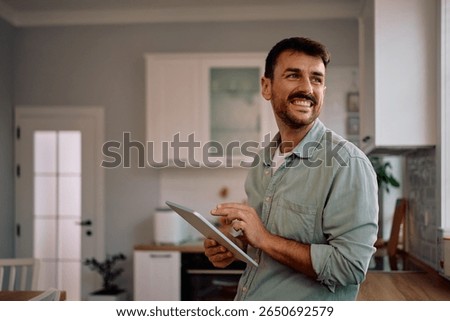 Happy man using digital tablet at home and looking away. Copy space.
