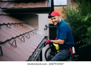 Happy man using leaf blower while cleaning gutters on the roof of a house. Copy space.