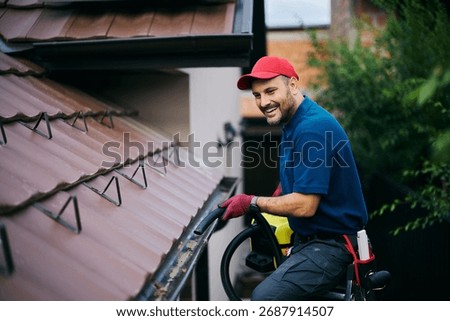 Happy man using leaf blower while cleaning gutters on the roof of a house. Copy space.