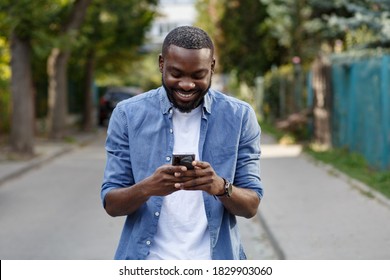 Happy man using mobile phone apps, texting message, browsing internet, looking at smartphone. Handsome Afro-American man using smartphone and smiling. Young people working with mobile devices.