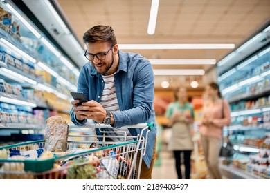 Happy man using mobile phone app while buying groceries in supermarket.  - Powered by Shutterstock