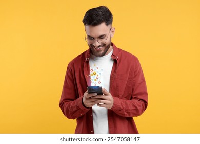Happy man using mobile phone on orange background. Different notification signs over gadget