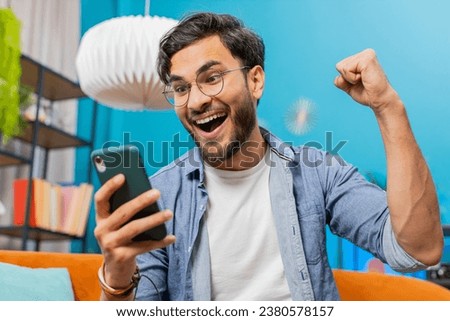 Happy man using mobile smartphone typing browsing say Wow yes, celebrating success victory, winning lottery jackpot goal achievement play game good positive news, triumph. Guy at home in room on sofa