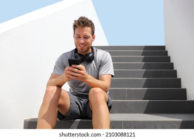 Happy Man Using Phone Outside Relaxing At Home Or Fitness Gym Listening To Audiobook With Wireless Headphones. Young People Lifestyle.