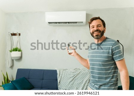 Happy man using a remote control to turn on the air conditioning while standing in his living room during a summer heatwave