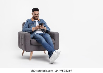 Happy man using smartphone in armchair on white background, space for text - Powered by Shutterstock