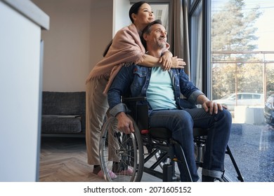 Happy man using wheelchair hugging with wife