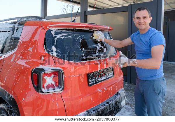 Happy man\
washes a car at a car wash. Car in\
foam