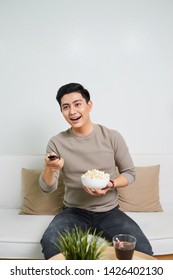 Happy Man Watching TV And Eating Popcorn Seated On A Sofa Isolated On White Background