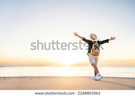 Happy man wearing hat and backpack raising arms up on the beach at sunset - Delightful man enjoying peaceful moment walking outdoors -  Wellness, healthcare, traveling and mental health concept