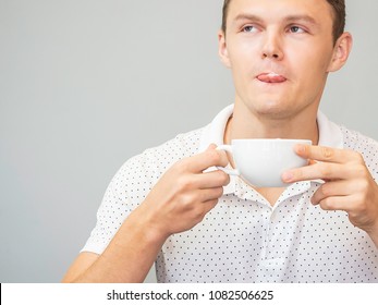 Happy Man In White Shirt And Holding Cup On Gray Background. Adult Drinking Cappuccino Coffee And Milk Froth On Mouth   .