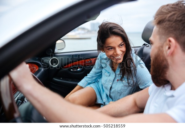 Happy man\
and woman driving in cabriolet car\
outdoors