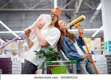 happy man and woman enjoy shopping, have fun, sing and dance holding mops, man with bucket on head, they laugh - Powered by Shutterstock