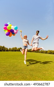 Happy man and woman holding balloons and jumping in the park