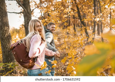 Happy Man And Woman Holding Hands Run Away Into Distance Along The Sunny Forest Path, Travelers Laughs Looking Back At Camera, Walking In Warm Sunny Day With Copy Space At Right Side