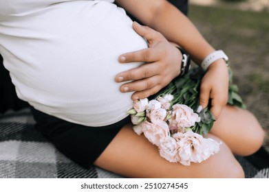 Happy man and woman, mother and father hugging pregnant belly while sitting on blanket with flowers outdoors. Close-up photo, pregnancy, motherhood. - Powered by Shutterstock