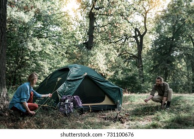 Happy man and woman putting up a tent in forest - Powered by Shutterstock