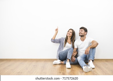 The Happy Man And Woman Sit On The Background Of The White Wall