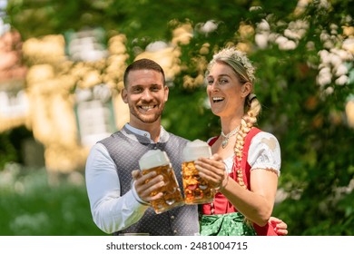 Happy man and woman in traditional Bavarian clothes, holding large beer mugs in a sunny outdoor setting at oktoberfest or beer garden in munich germany,  - Powered by Shutterstock