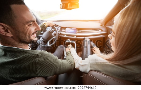 Happy man and woman\
traveling in car. Back view of beautiful young couple sitting on\
front passenger seats and smiling while handsome man driving\
comfortable automobile.
