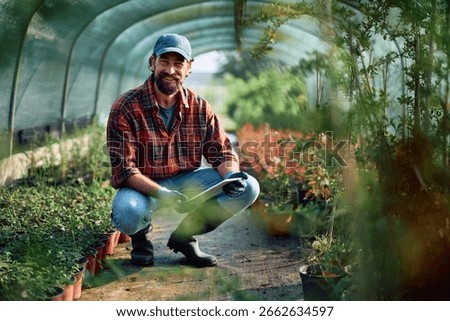 Happy man worker using touchpad while working at plant nursery and looking at camera. Copy space. 