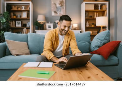 Happy man working from home on a laptop in a cozy living room