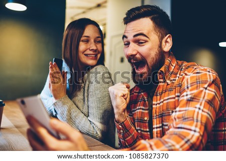 Happy marriage celebrating victory in internet lottery watching online broadcast on smartphone with winning results.Amazed hipsters wondered with win in online auction betting on website on phone