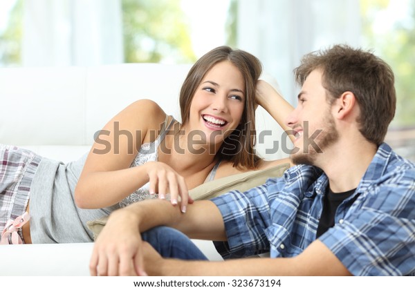 Happy marriage or couple flirting and laughing lying\
on a couch at home