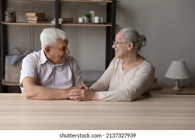Happy marriage, eternal love, trustworthy harmonic relations between older spouses concept. Senior grandparents sit at table at home smile look at each other hold hands feel endearment, express caress