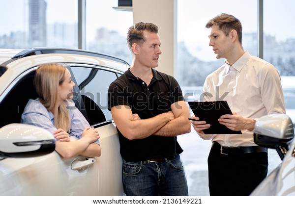 happy\
married couple choosing and buying car at car showroom. Car\
salesman helps them to make right decision. caucasian man and woman\
have talk with consultant manager of auto\
showroom