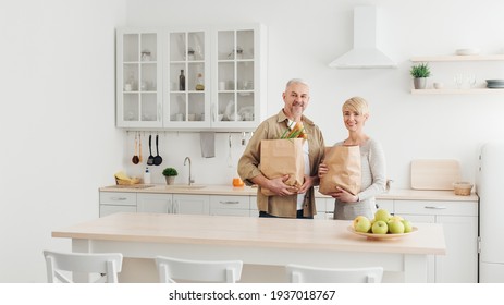 Happy married couple coming home from shopping and unpacking paper bags with groceries in kitchen together - Powered by Shutterstock